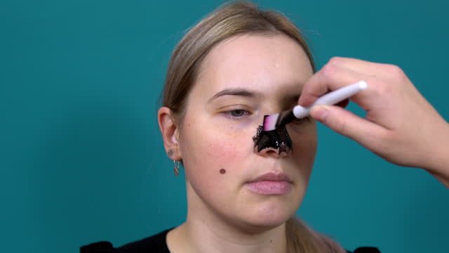 A woman is given a black nose mask against black dots on the skin