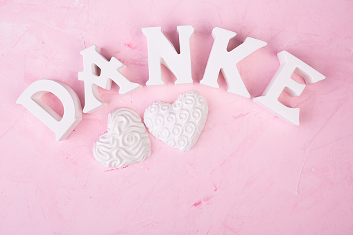 german thank you letters and two ceramic hearts on pink background, flat lay
