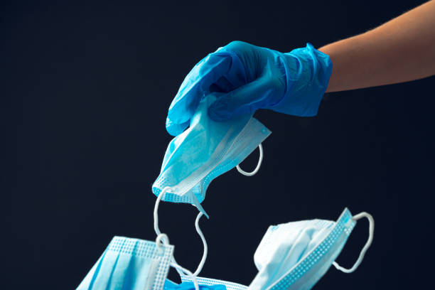 istock Hand putting used dirty surgical mask to a garbage bin. 1291976193