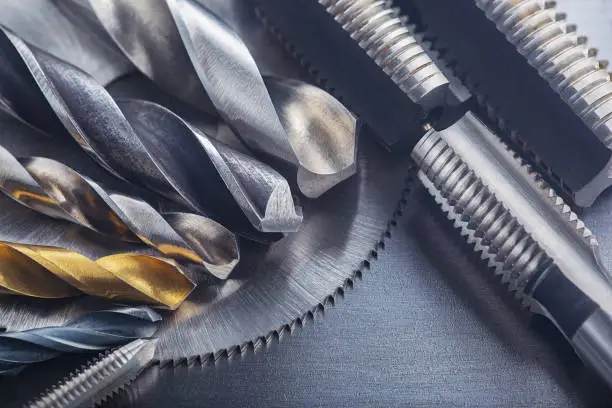 Photo of set of different drill bits,thread tap and mill cutters on steel plate background. Locksmithing deal.