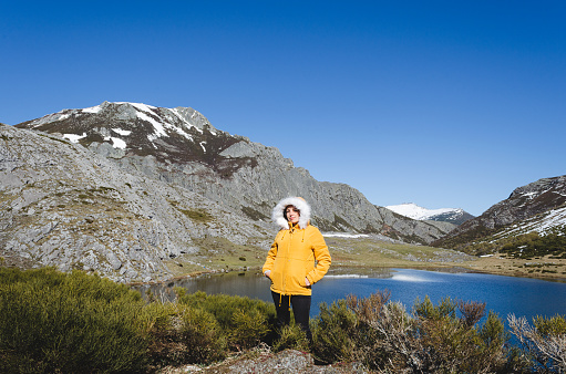 Mountain landscape with snowy mountains and lake. Woman in yellow jacket looking at camera. Lake Isoba, Leon. Spain.