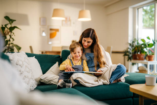 Mother and son reading a book Young mother with her preschool kid reading a children's book on a sofa. They are having a nice time and are smiling. Modern house, daytime. Horizontal photo, copy space parent and child reading stock pictures, royalty-free photos & images