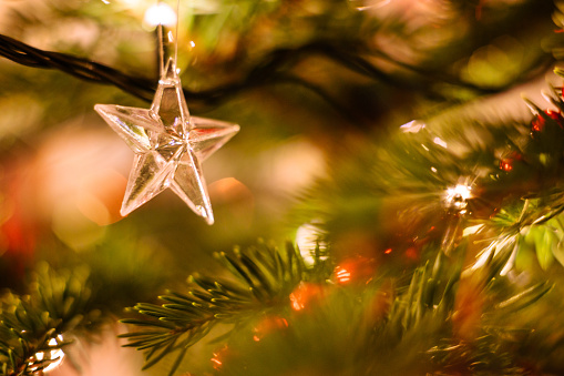 A glass star swinging on a christmas tree with glittering lights and blurred needles in background.