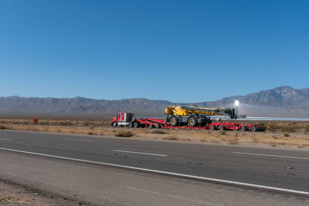 istock Long Haul Semi Truck Pulling a Large Tractor on A Two Way Highway 1291987565