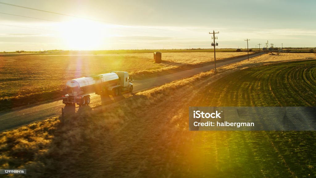 Aerial Shot of Milk Tanker on Country Road with Dramatic Lens Flare Aerial shot of a milk tanker driving along a road between dairy farms, collecting milk in the evening. Dairy Farm Stock Photo