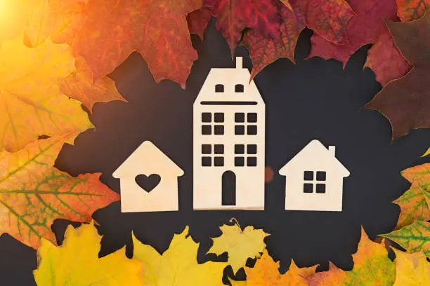 Photo of on a black background - three different wooden houses surrounded by autumn leaves. Concept - Autumn sales, year-end sales, affordable housing, mortgage discounts, real estate investments.