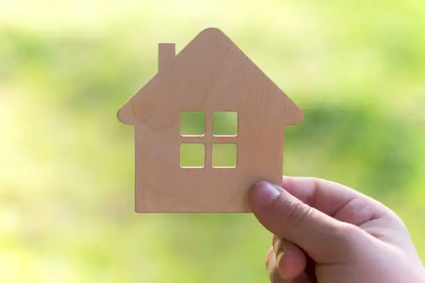 Photo of toy wooden house in hand on a light green background, Concept - buying a house on credit or mortgage, safe and affordable housing. My home is my castle. safety
