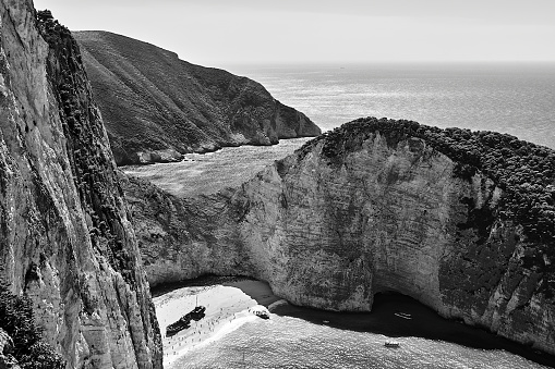 Rocky cliffs, shipwreck and people on the beach Navagio on Zakynthos island in Greece, monochrome