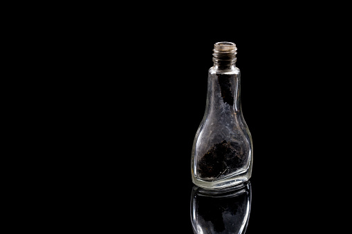 A single dirty vintage perfume bottle on a reflective black background with copy space.