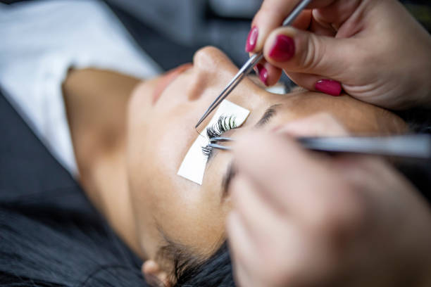Female eye with long lashes. Eyelash extension procedure. Eyelashes, close-up, macro, selective focus A beautician applies artificial eyelashes to a client in a beauty salon with work tools in her hands, the concept of beauty treatment Woman Eye with Long Eyelashes. Beauty treatment, applying false eyelashes false lashes stock pictures, royalty-free photos & images
