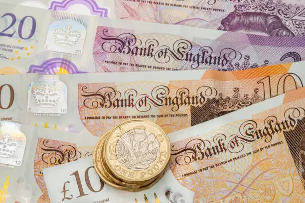 Photo of UK one pound coins placed on a background of UK banknotes