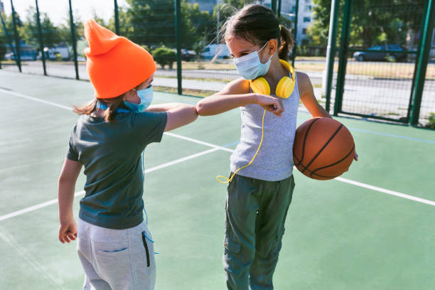 Two children with face protective masks using new style handshakes and greetings