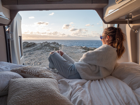 Road trip concept, woman living the van life experience watching stunning view while lying on the bed of the back of her camper