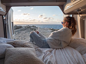 Woman lying at the back of a van looking at ocean