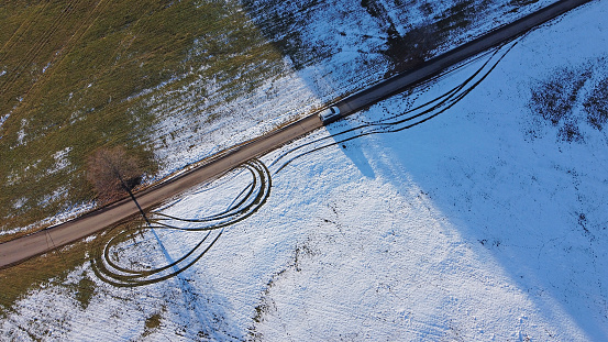 Drone photo of white car driving from light to shadow on road in winter