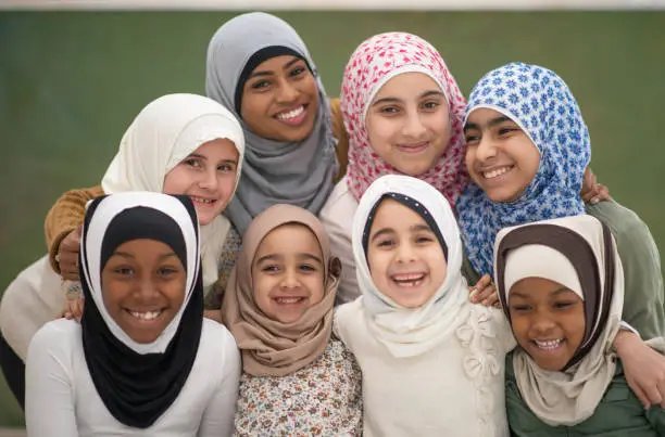 A very happy group of Muslim students posing with their teacher. They are all wearing a hijab or headscarf.