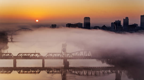 sun rising over little rock mientras el tren de carga cruza el río - aerial - freight train railroad track train rock fotografías e imágenes de stock