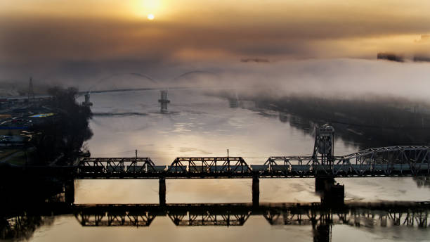 el sol en ascenso se asoma a través de la niebla gruesa mientras el tren de carga cruza el puente junction en little rock, arkansas - aerial - freight train railroad track train rock fotografías e imágenes de stock