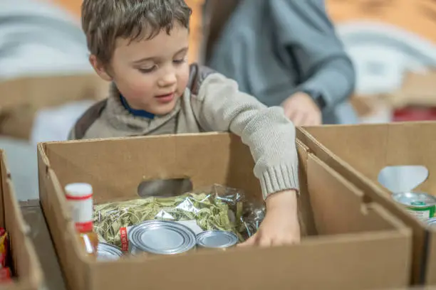 Young boy volunteering with his mother at a food bank.