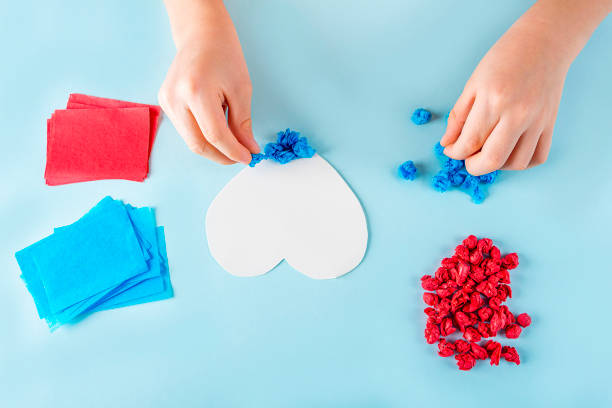 istock Concept of DIY and kid's creativity. Step by step instruction: make  heart. Step3 Child's hands stick crumpled pieces of paper on adhesive heart template. Valentine's Day craft. Fine motor skills 1292041021