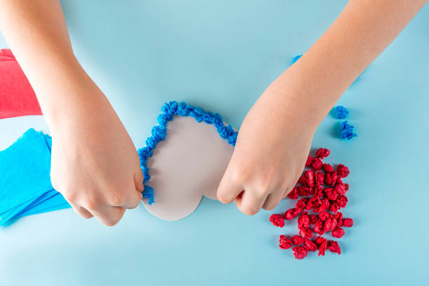 istock Concept of DIY and kid's creativity. Step by step instruction: make  heart. Step3 Child's hands stick crumpled pieces of paper on adhesive heart template. Valentine's Day craft. Fine motor skills 1292041025