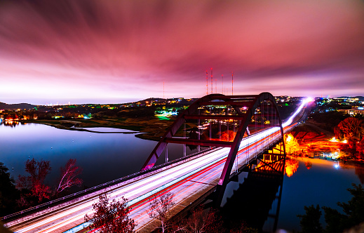 Pennybacker Bridge the Historic Austin Texas Landmark over the Colorado River , 360 Bridge Night Time lapse Long Exposure Brilliant Night Colors with headlights and brake light trail over the suspension bridge with Pink Cloud colors and Austin Cityscape in the background and the Texas Hill Country