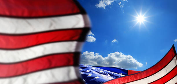 istock Waving American flag over blue sky with shinning sun 1292048877