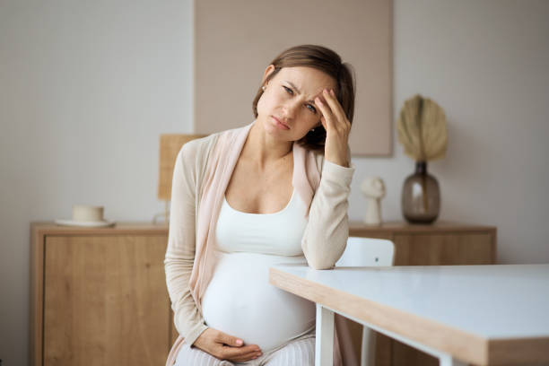 Pregnant woman suffering from headaches while sitting at the table stock photo
