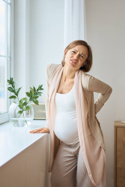 Healthcare, treatment. Young pregnant woman feeling sudden pain in her back. Future mom suffering from backpain. stock photo