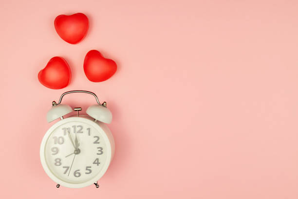 istock Pink Background with white alarm clock and red hearts. Creative layout. Top view. Time for love and greetings. 1292057637