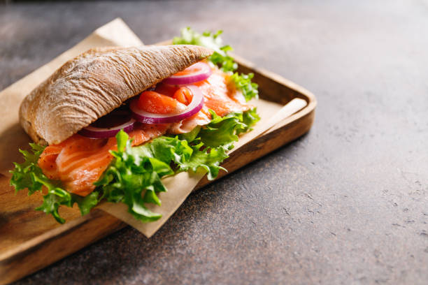 sandwich sain avec pain de seigle, saumon, avocat, oignon et salade servi sur une planche rustique en bois. - gourmet salad dinner prepared fish photos et images de collection