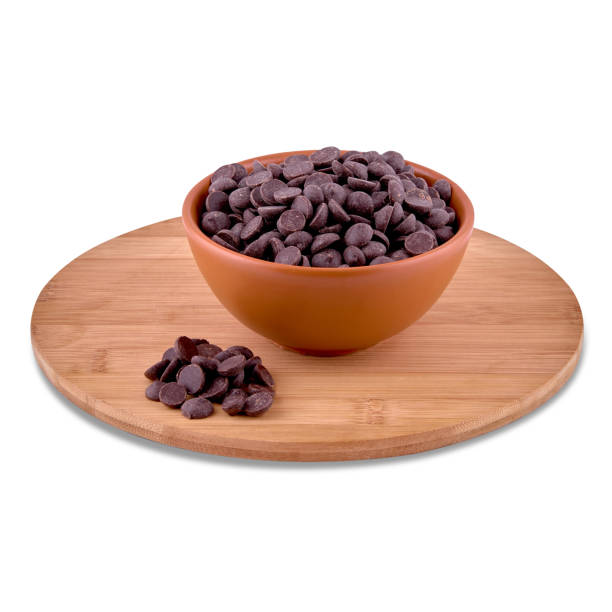 istock Candy dark chocolate drops in brown ceramic bowl on wood board isolated on white background, copy space. 1292065407