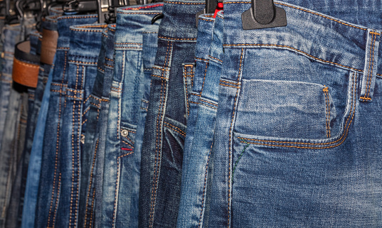 Close up shot of various blue Jeans on a hanging rack in the clothes store. Shopping and clothing store concepts.