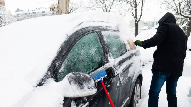 駐車場で雪に覆われた車。男は車からスナックをきれいにします。 - snow car window ice scraper ストックフォトと画像