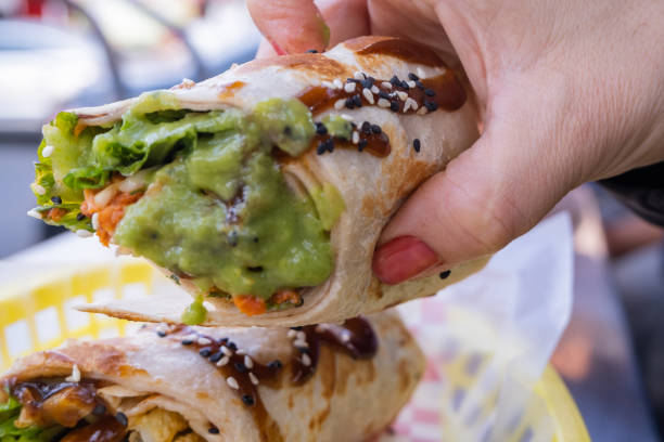 istock Female hand holding a burrito covered with guacamole 1292070386