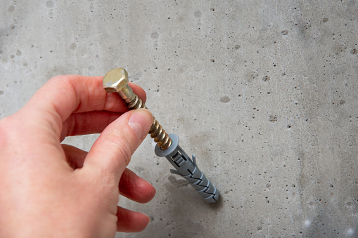 Hand holds a gray screw on the background of a gray concrete wall close-up, top view, copy space. Hardware, fasteners and materials for construction and repair