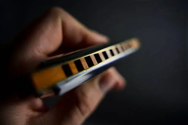 Harmonica being held in ready position to play under a dramatic light and blurred