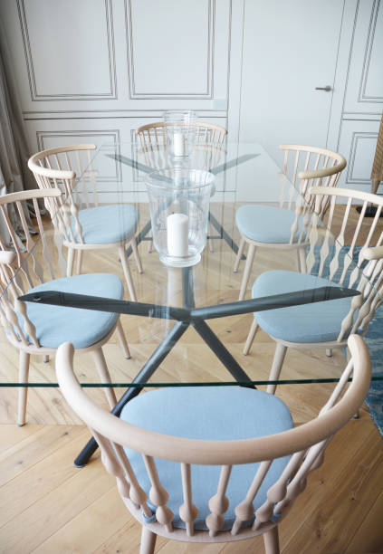 istock A modern tempered glass rectangular dining table with stainless steel cross legs and blue admiral armchairs with wood backs. 1292089582