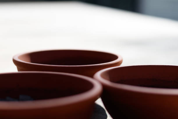 Three empty terracotta plant pots on a table in an outdoor table under sunshine, casting shadows