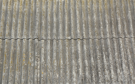 A close-up on simple roofing, old dangerous for health asbestos cement roof sheets installed on the rooftop of the house.