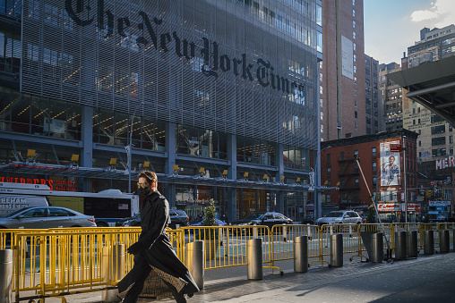 Manhattan, New York. December 15, 2020. A man wearing a mask walks in front of New York Times building on 8th avenue in Midtown.