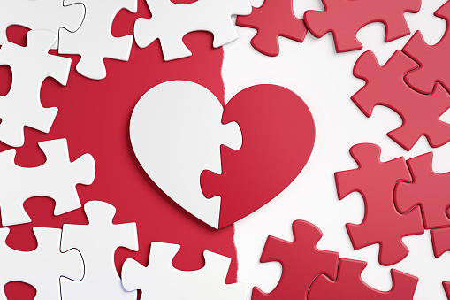 Jigsaw puzzle in form of a heart symbol is composed from two halves, which are placed amongst ordinary pieces of another jigsaw puzzle. 3D rendering graphics.