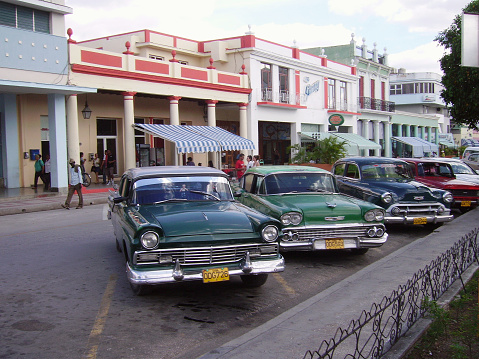 Local people Walking on the central square in Holguin, by some beautiful vintage american cars, Cuba