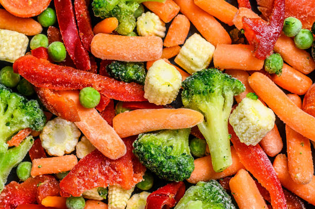 istock Frozen cold sliced Vegetables, broccoli, sweet peppers, tomatoes, carrots, peas and corn. Black background. top view 1292101243