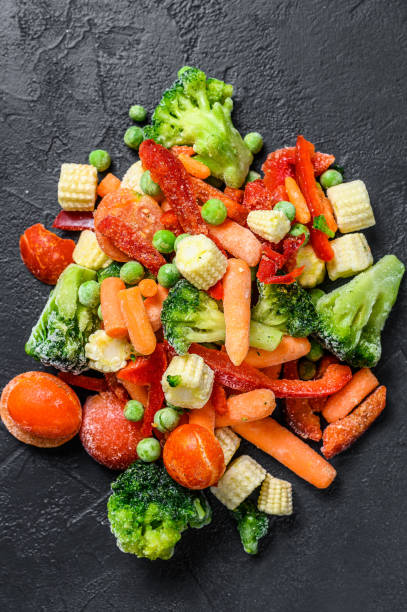 istock Frozen cold sliced Vegetables, broccoli, sweet peppers, tomatoes, carrots, peas and corn. Black background. top view 1292101255