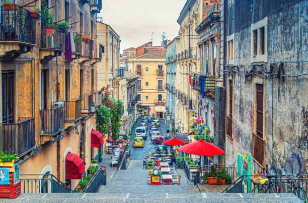 Narrow street with stairs, old buildings with balconies and street restaurants with tents and umbrellas in Catania stock photo