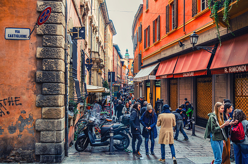 Bologna, Italy, March 17, 2019: people are walking down typical italian street with buildings with bright colorful walls in old historical city centre, Emilia-Romagna