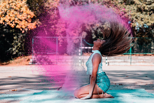Cheerful young urban woman having fun and playing with colored powder in the sports court in the city outdoors