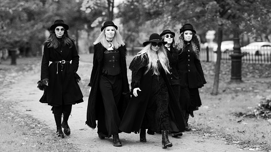 Five women as witches go to the Sabbath, a group of witches or Goths in black clothes and hats go down the street