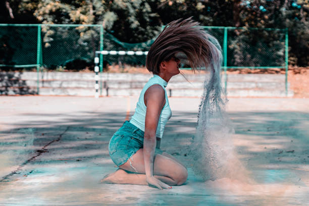 Young playful woman with long hair having fun with colored powder in the sport court in the city outdoors on a lovely summer day